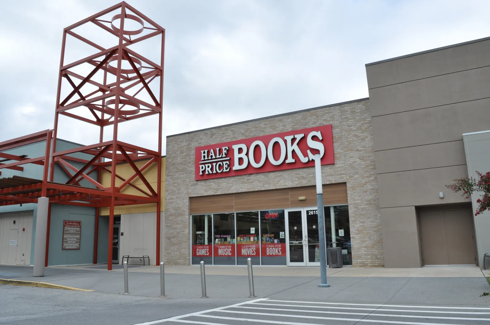 Half Price Books store exterior with large red and white sign and metal architectural feature against a cloudy sky.
