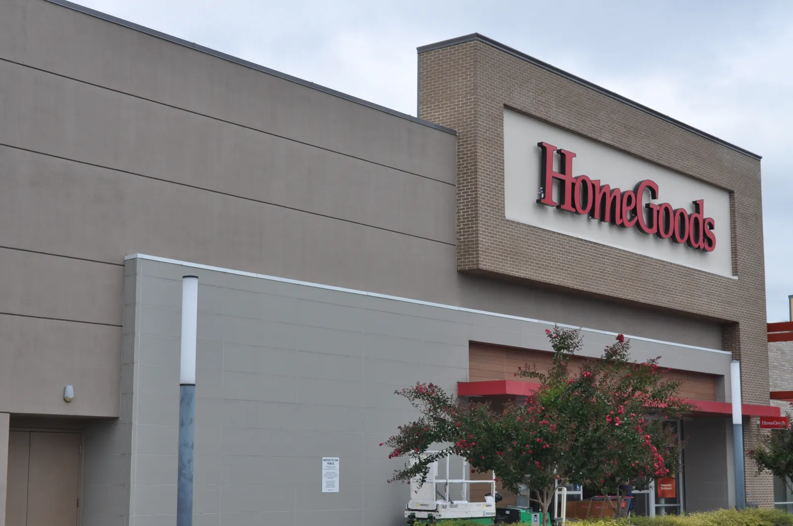 Exterior view of HomeGoods store with large red sign and landscaping including flowering trees.