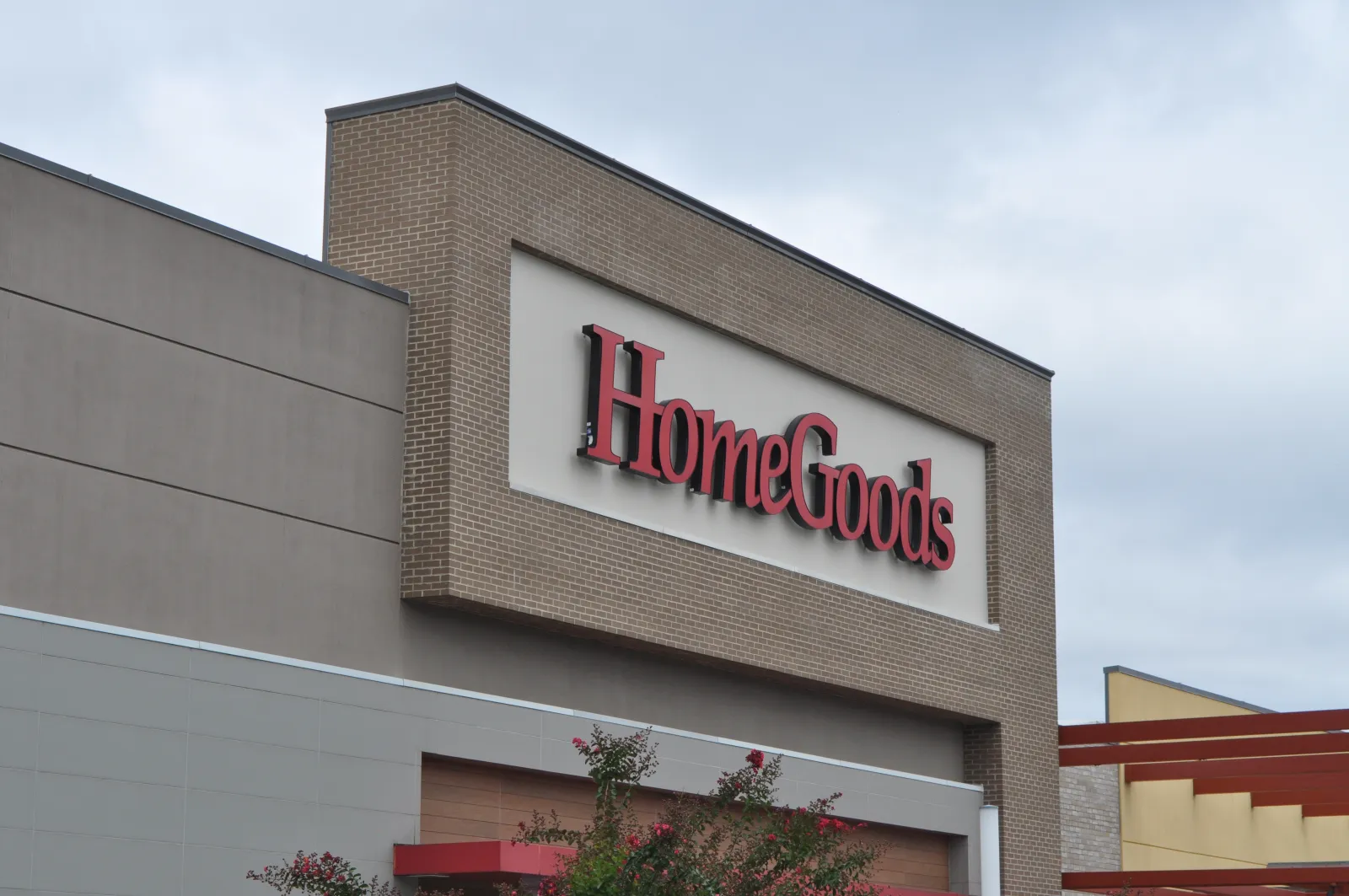 Exterior view of a HomeGoods store sign on a brick and beige building under a cloudy sky.