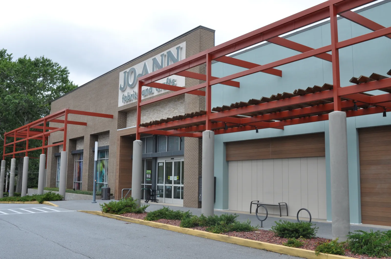 Exterior of a Joann Fabrics and Crafts store with red metal framework and glass windows on a cloudy day