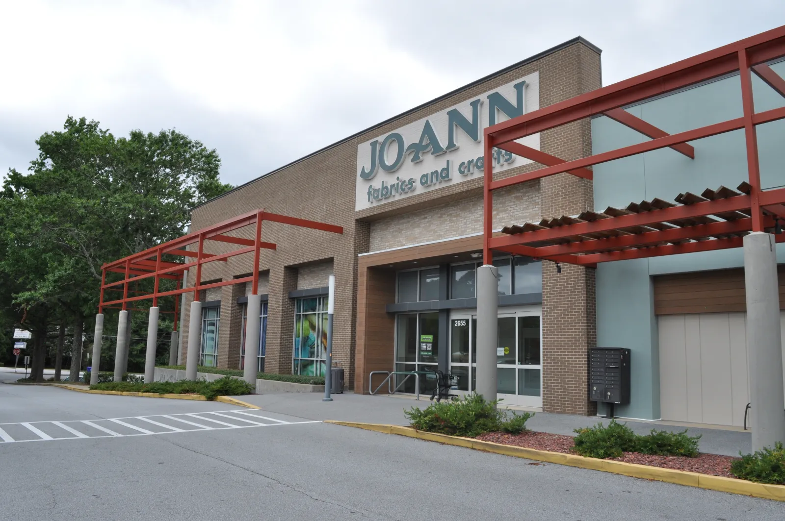 Exterior view of JOANN fabrics and crafts store with brick facade and red pergola on a cloudy day