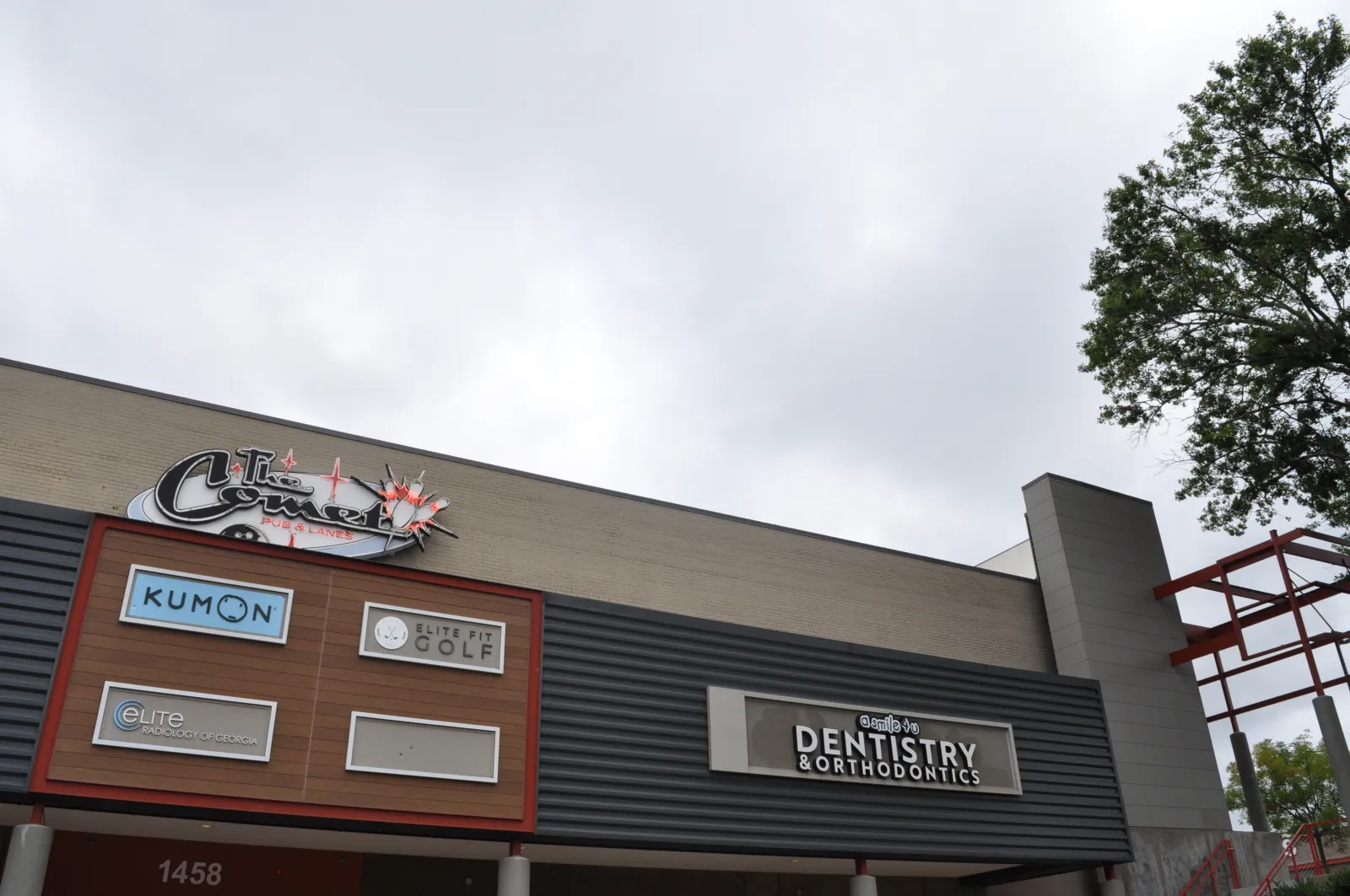 Commercial building facade featuring signs for Kumon, Elite Fit Golf, dentistry, and other businesses under a cloudy sky.