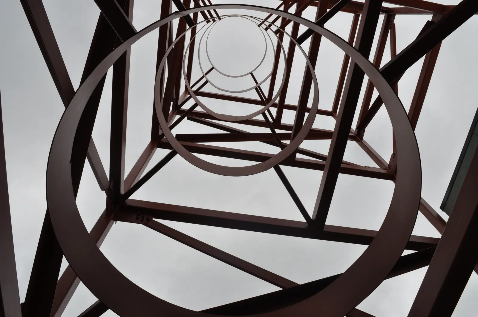 View looking up through circular metal rings of a tall industrial tower against a cloudy sky