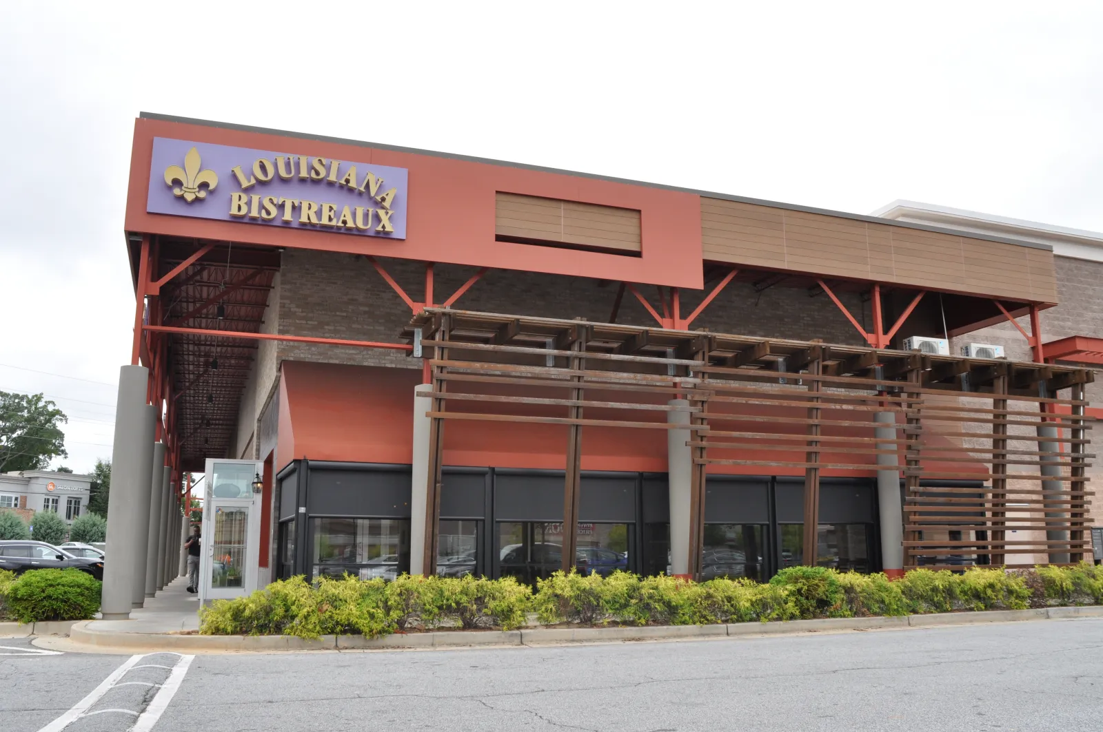 Exterior view of Louisiana Bistreaux restaurant with red accents and green landscaping in front.