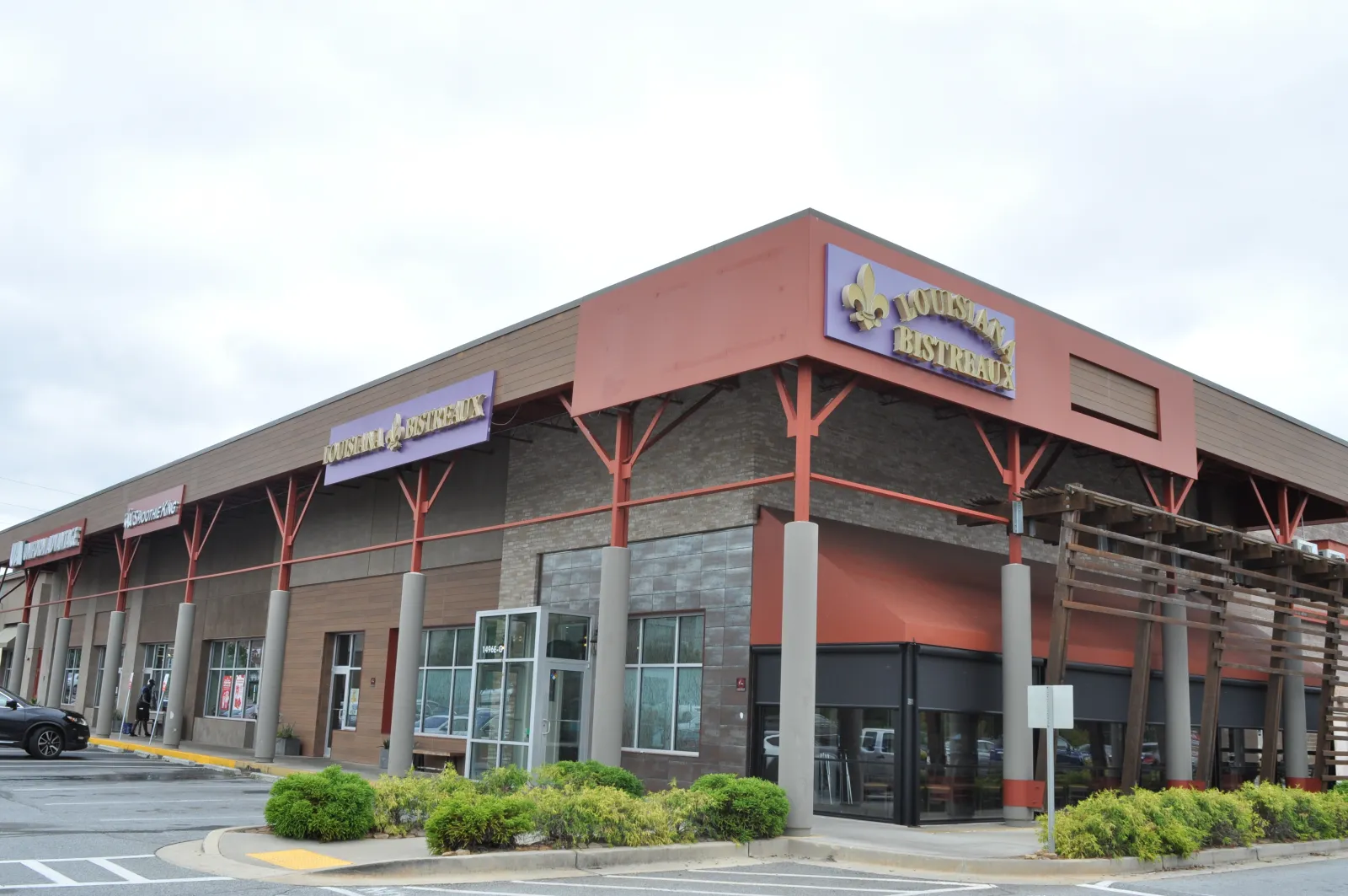 Corner view of a shopping plaza with Louisiana Bistreaux restaurant and various stores under a cloudy sky.