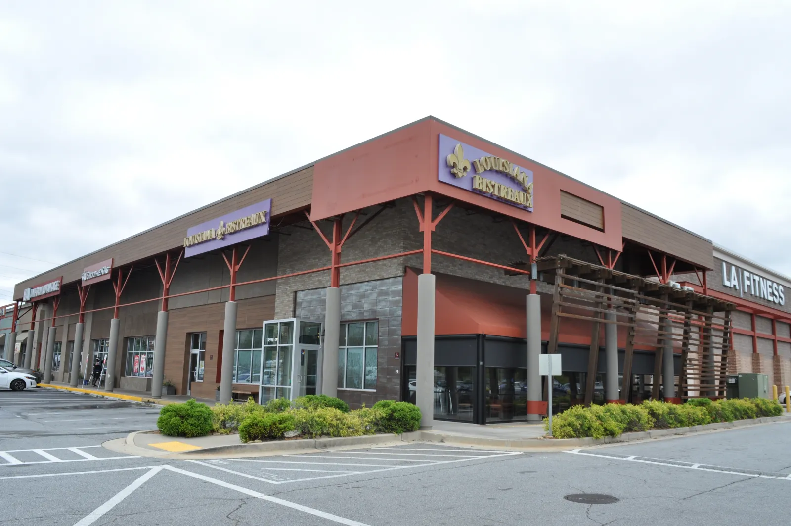 Exterior view of a shopping plaza featuring LA Fitness and Louisiana Bistreaux restaurants on a cloudy day.