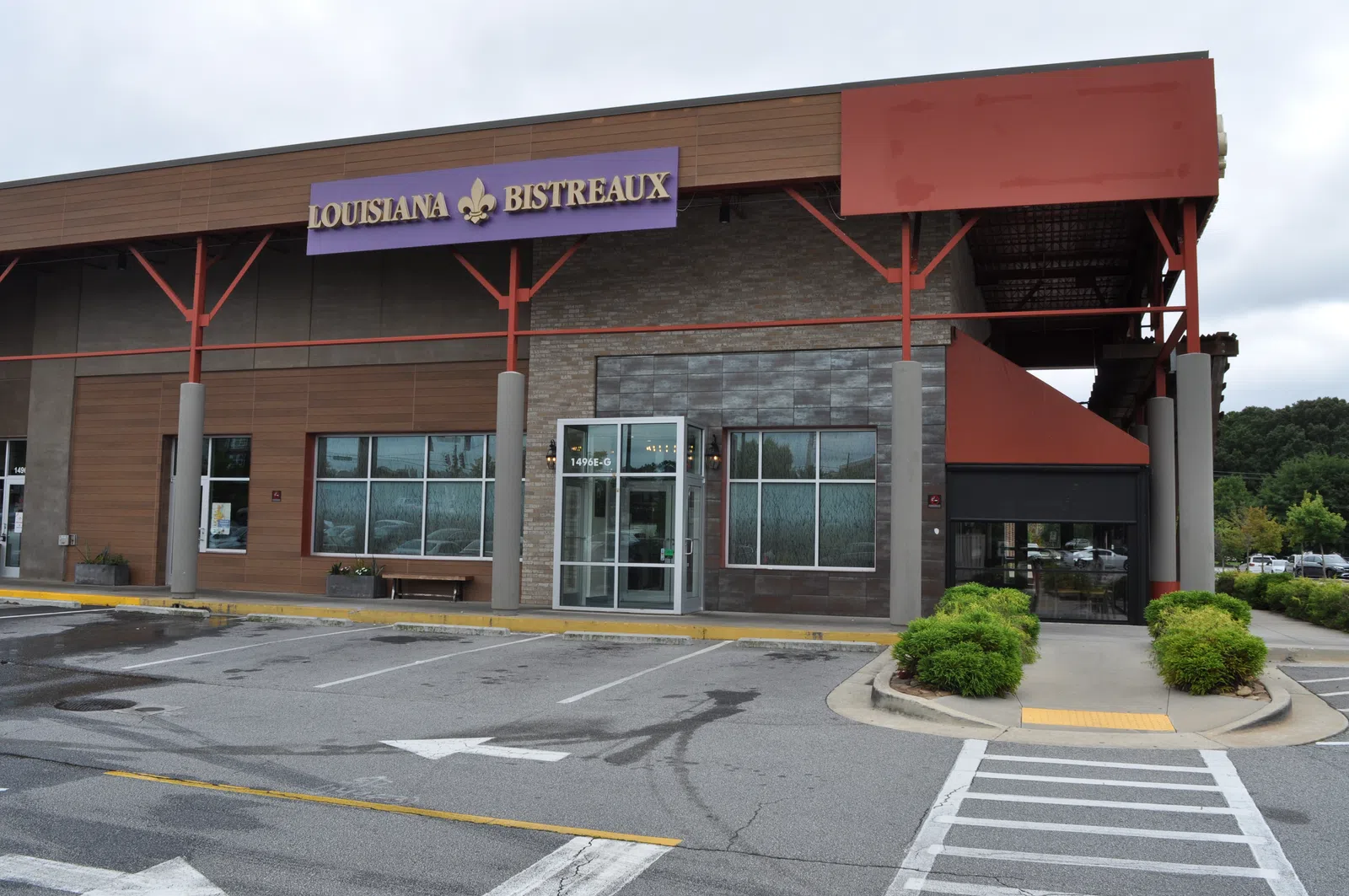 Front view of Louisiana Bistreaux restaurant with empty parking lot and greenery under cloudy sky.