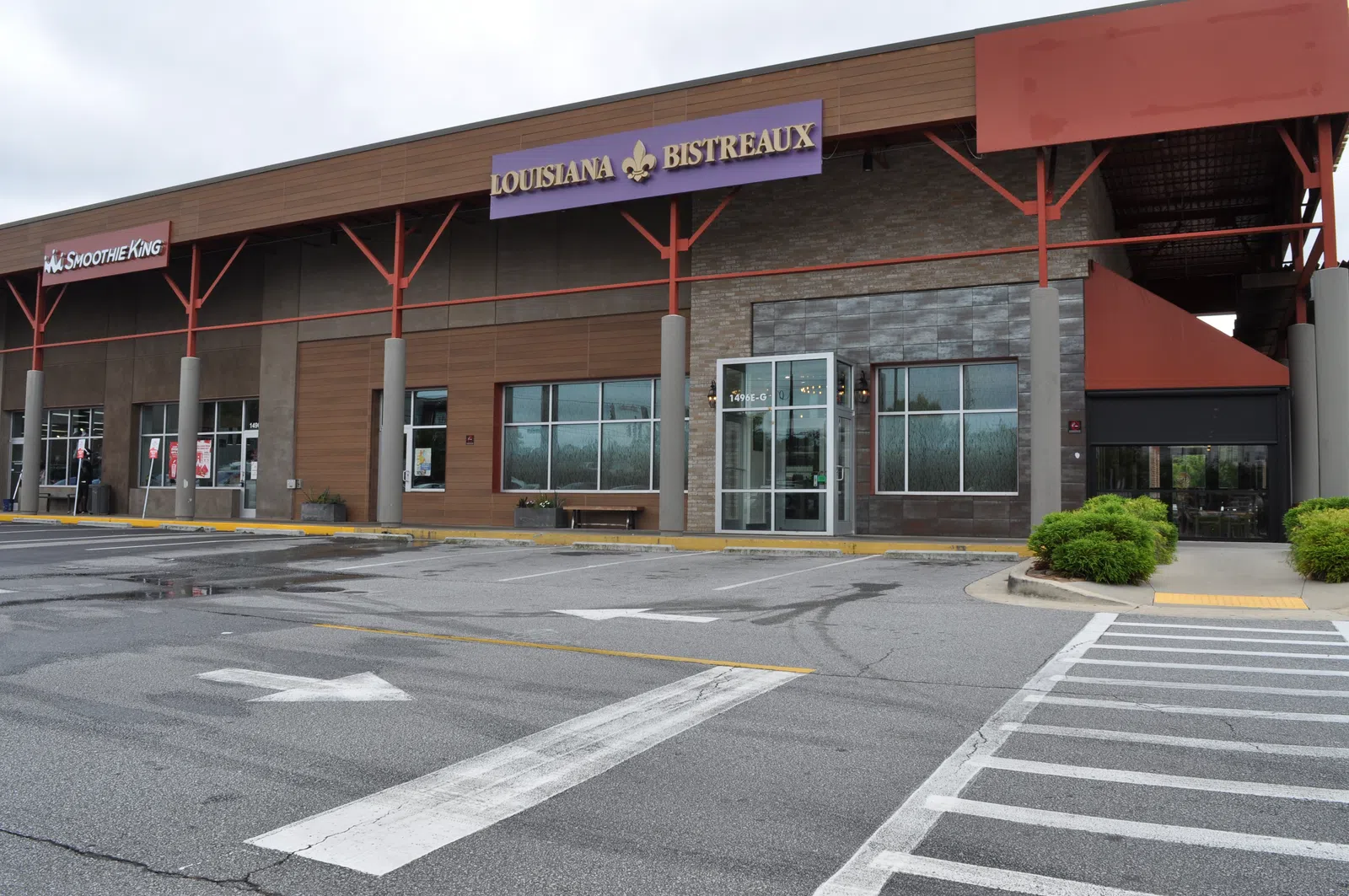 Empty parking lot outside a shopping plaza featuring Louisiana Bistreaux and Smoothie King storefronts under an overcast sky