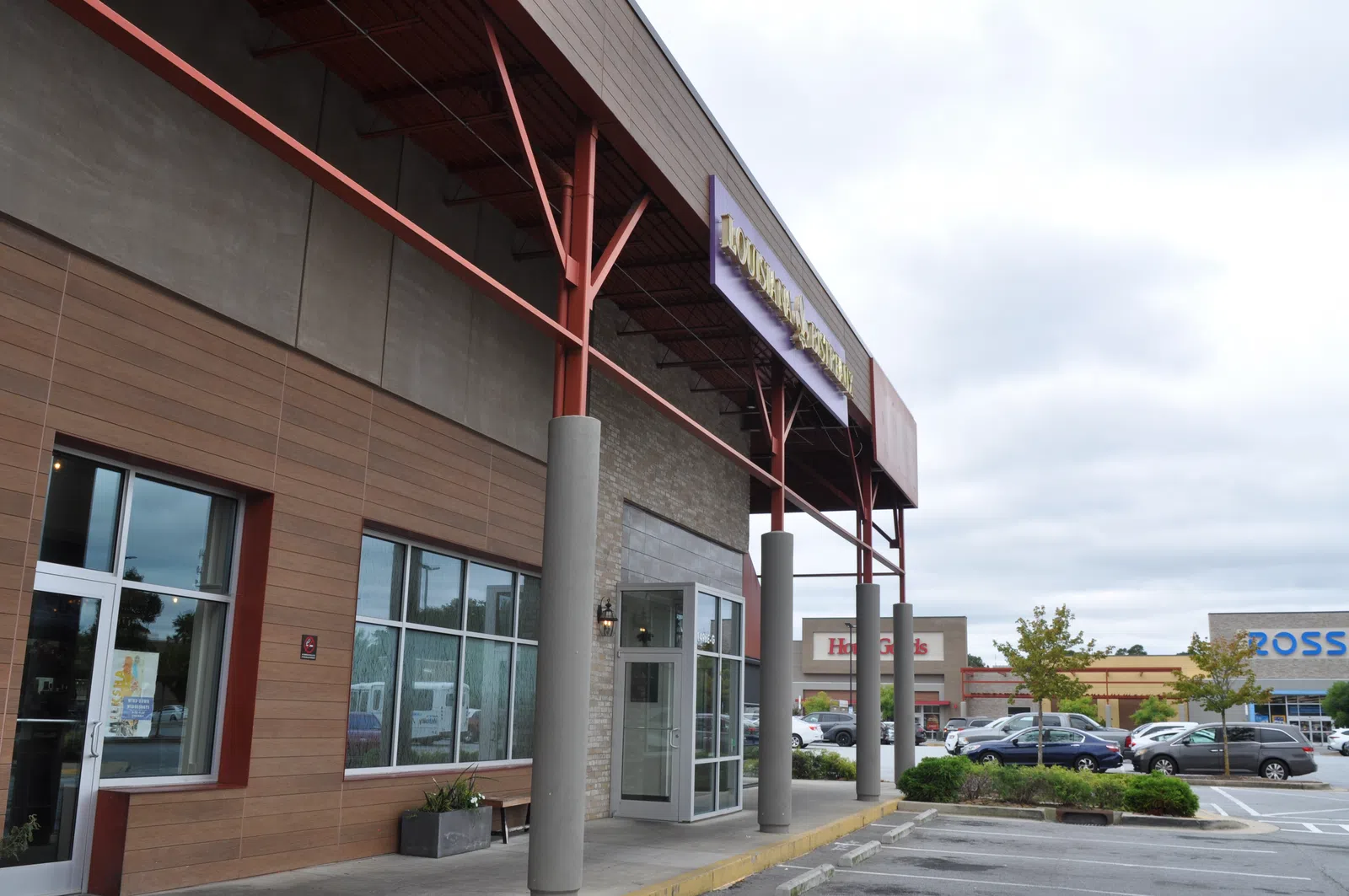 Exterior view of a shopping plaza with a restaurant entrance and nearby stores including Ross and Hobby Lobby.