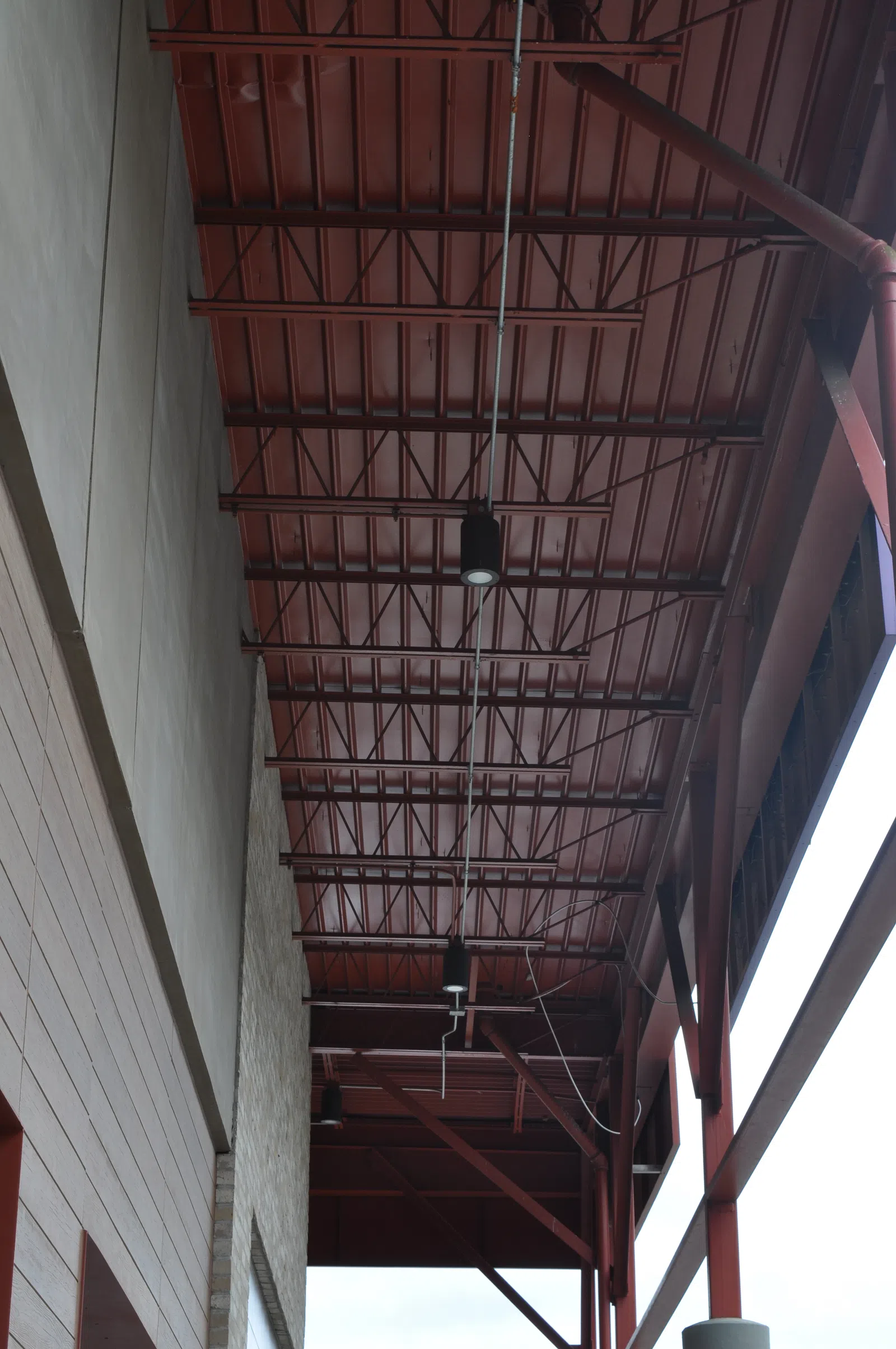 View of industrial red metal ceiling with pipes and lighting fixtures under an open structure