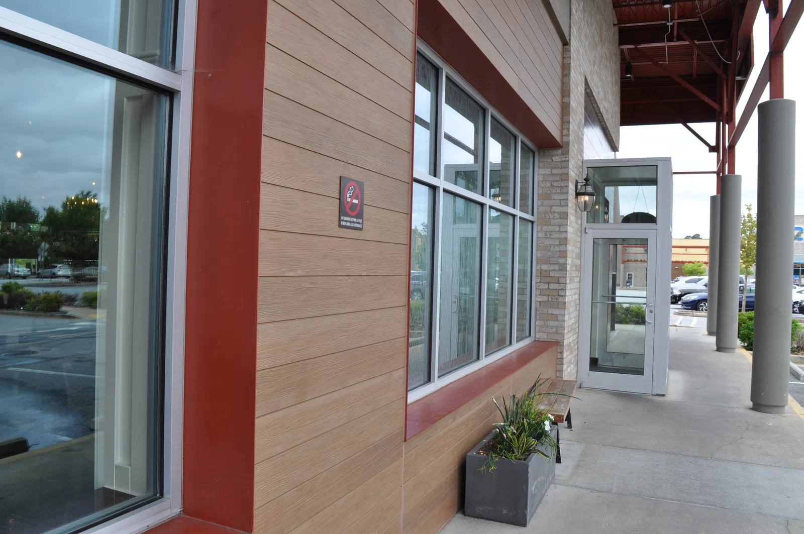 Modern building exterior with large windows, planter box, and an entry door under a covered walkway.