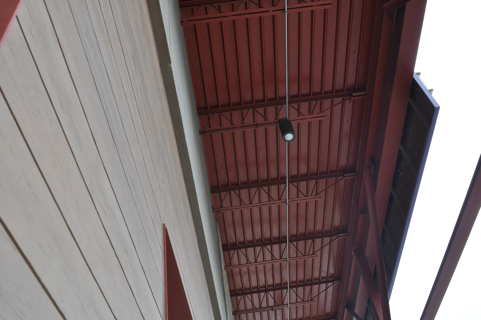 View looking up at a modern building's red metal ceiling and adjacent light-colored wood panel wall with a ceiling light fixture.