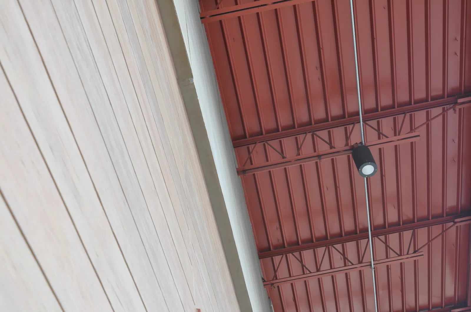 Wood paneled wall beside a red industrial ceiling with exposed beams and a hanging spotlight.