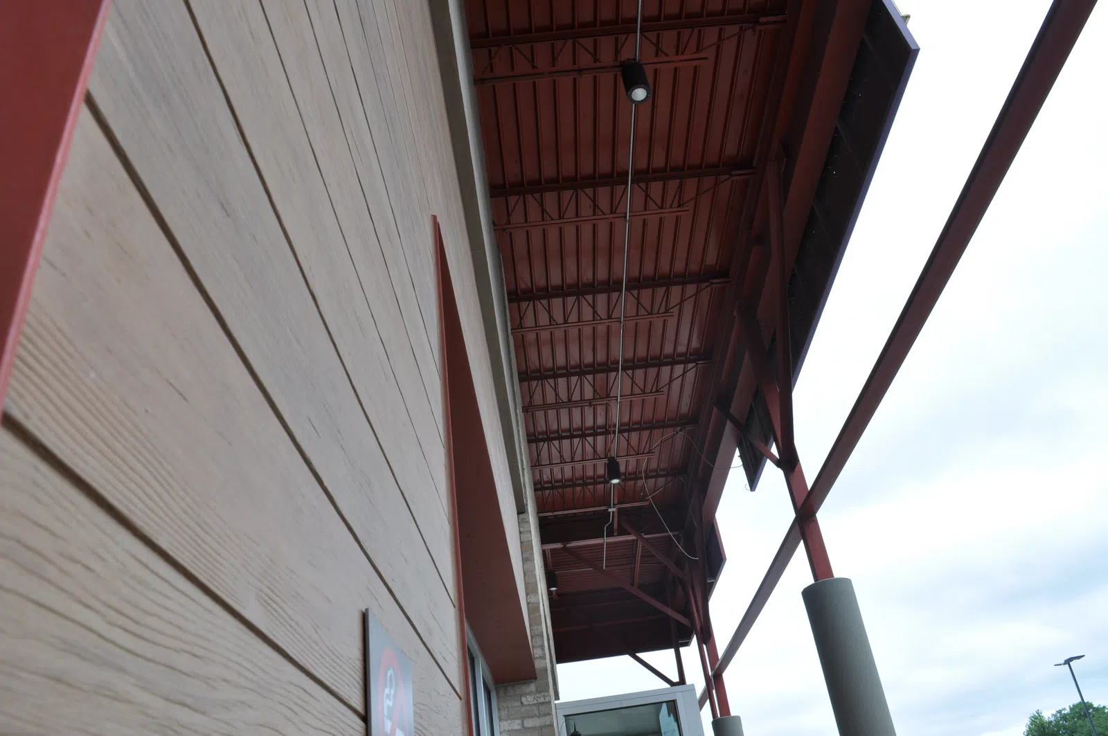 View of angled building exterior with beige siding and brown metal roof structure against cloudy sky.