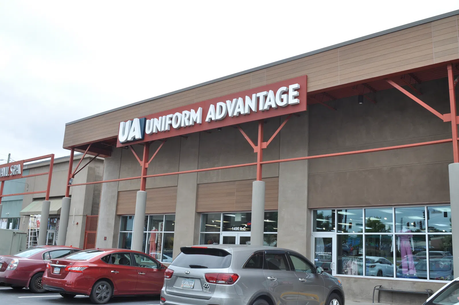 Exterior view of Uniform Advantage store with cars parked in front under overcast sky.