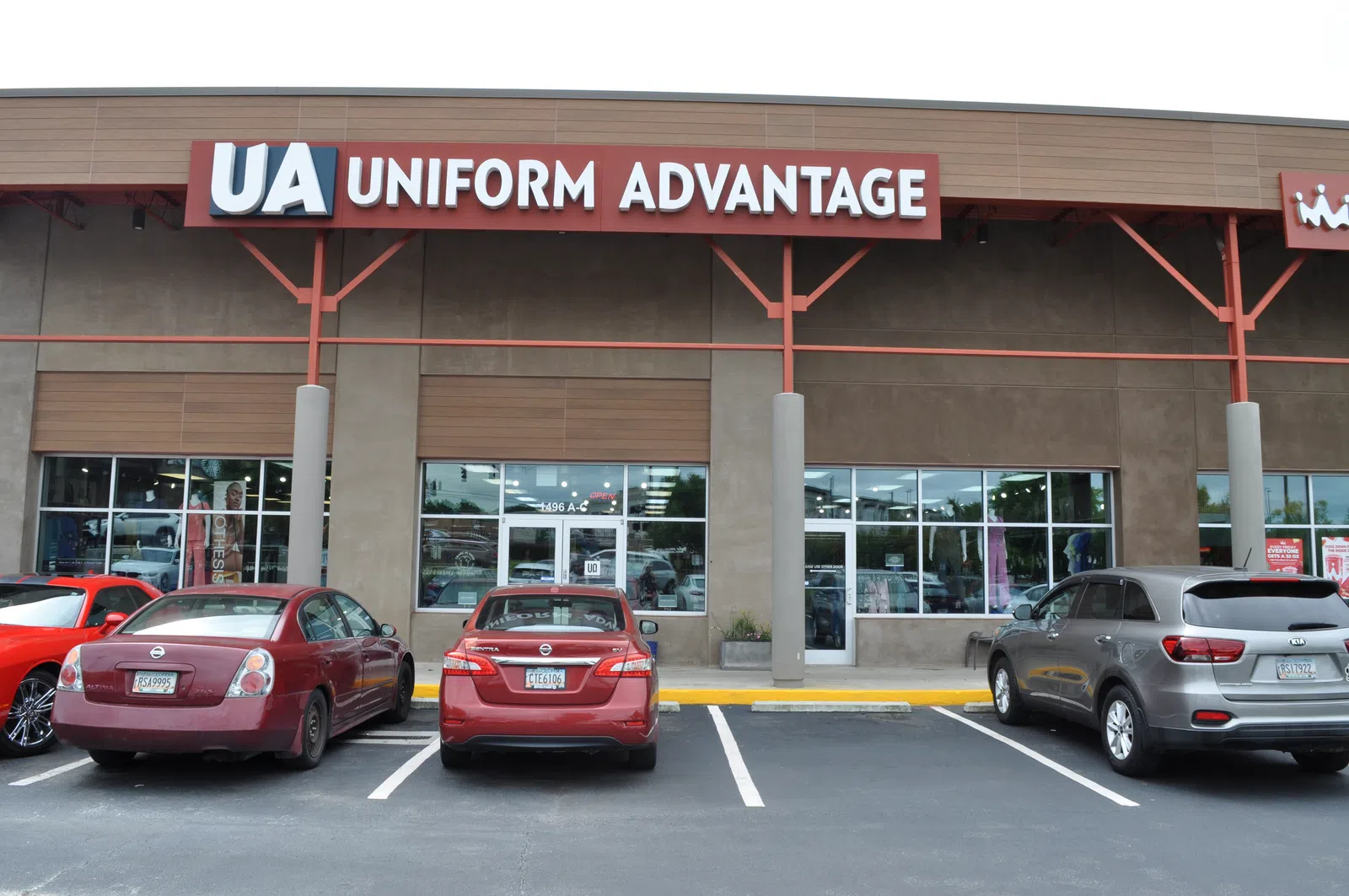 Storefront of Uniform Advantage with red and gray vehicles parked in front under clear sky.