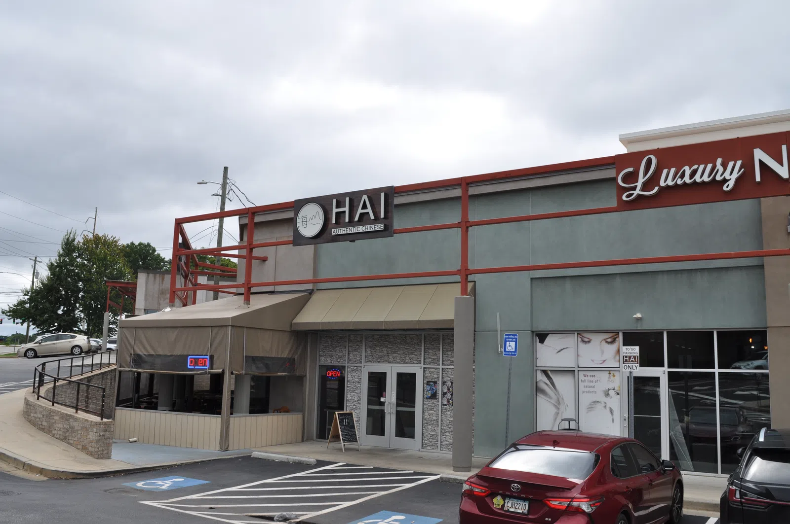 Exterior view of a nail salon with signage, parking spaces, and a red car under a cloudy sky.