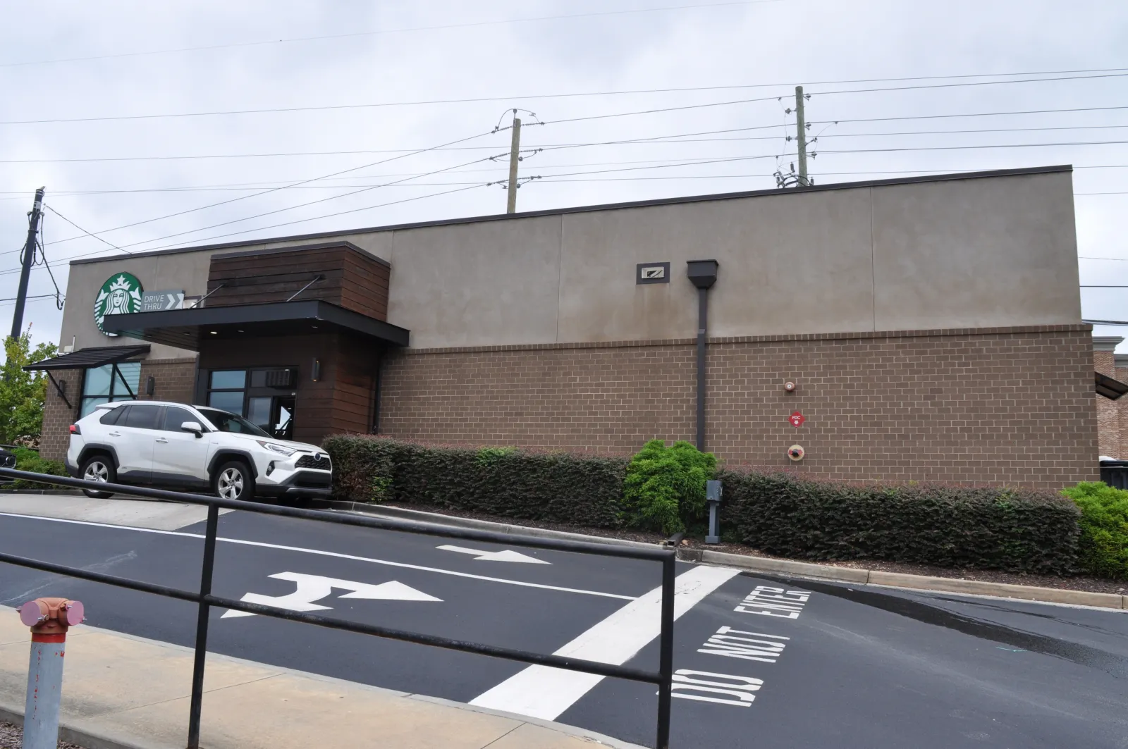 Exterior view of a Starbucks coffee shop with a white SUV parked and directional arrows on the road.
