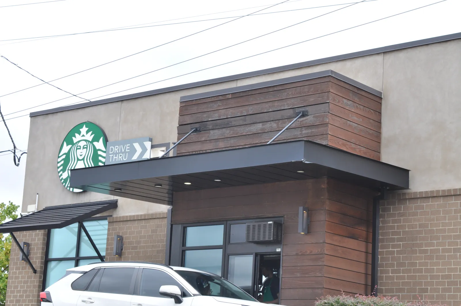 Starbucks coffee shop exterior with drive-thru lane and a white SUV parked nearby during daytime.