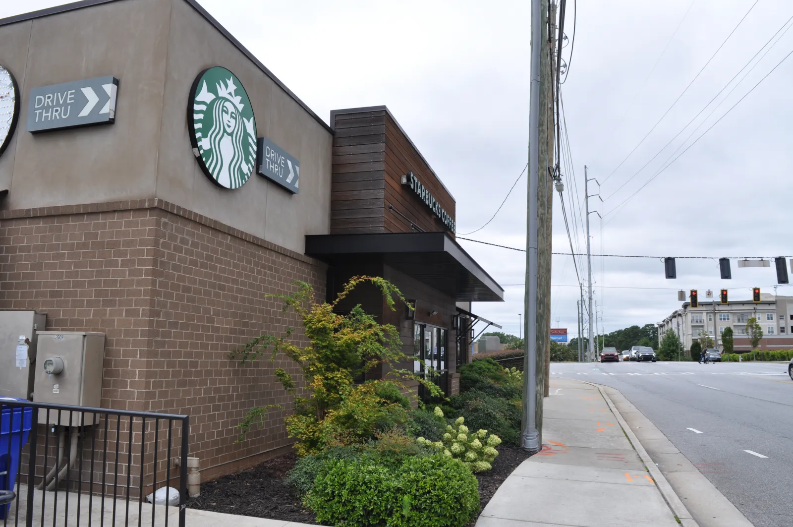 Exterior view of a Starbucks coffee shop with drive-thru signs and a nearby street intersection on a cloudy day