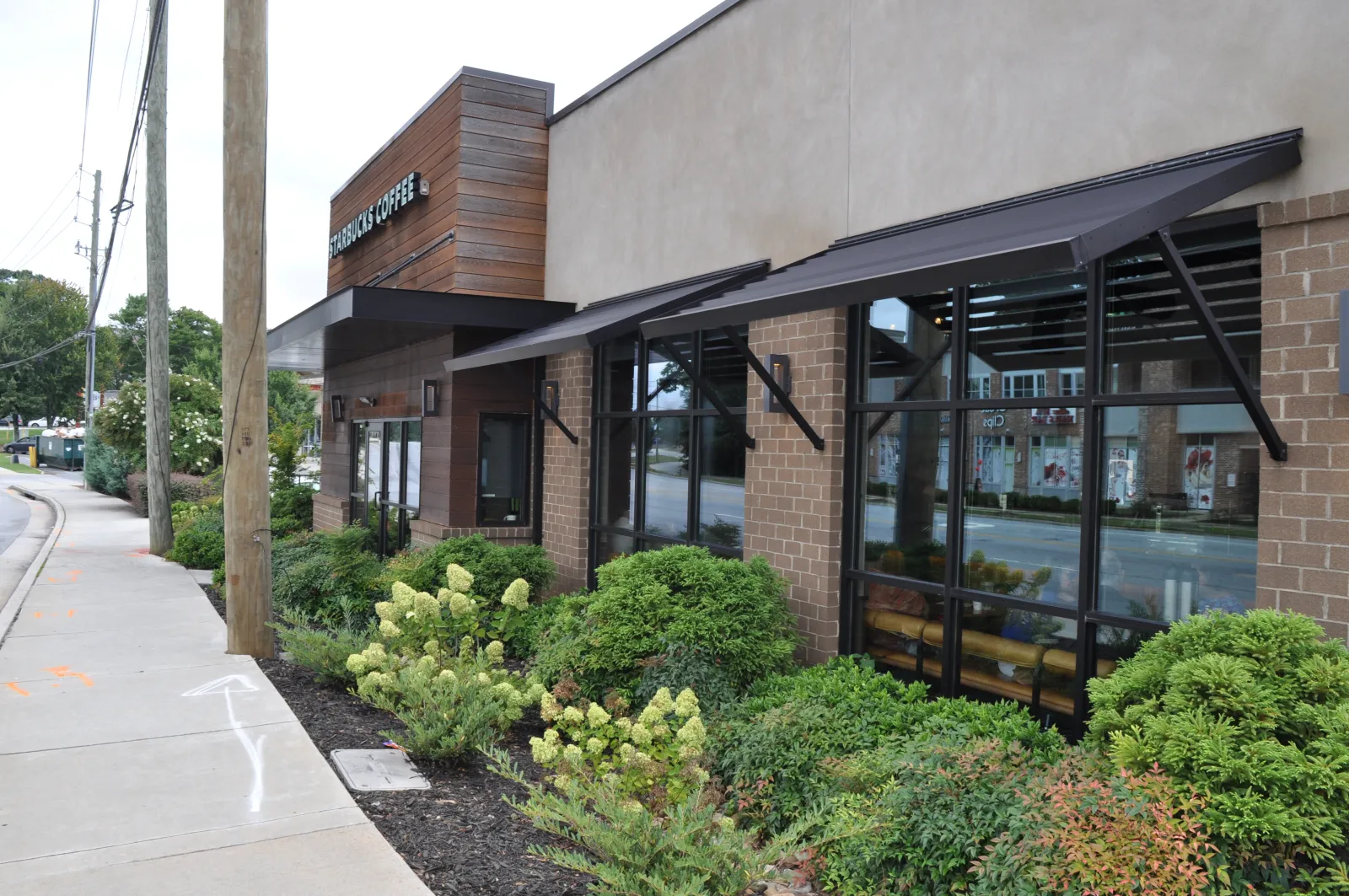 Starbucks Coffee shop exterior with large windows, awnings, and landscaped greenery along the sidewalk.