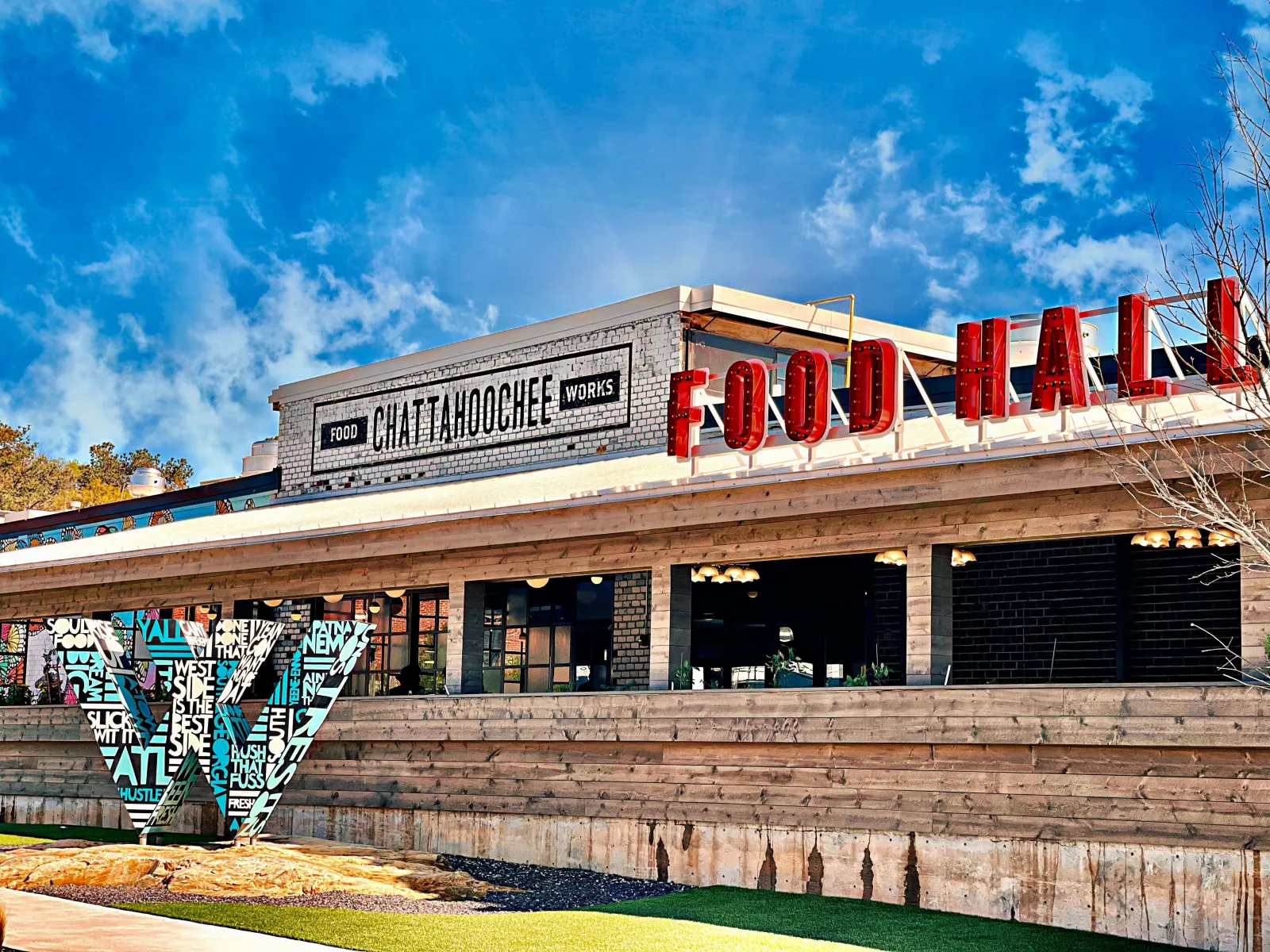 Exterior of Chattahoochee Food Works Food Hall with large bold signage and artistic installation under blue sky