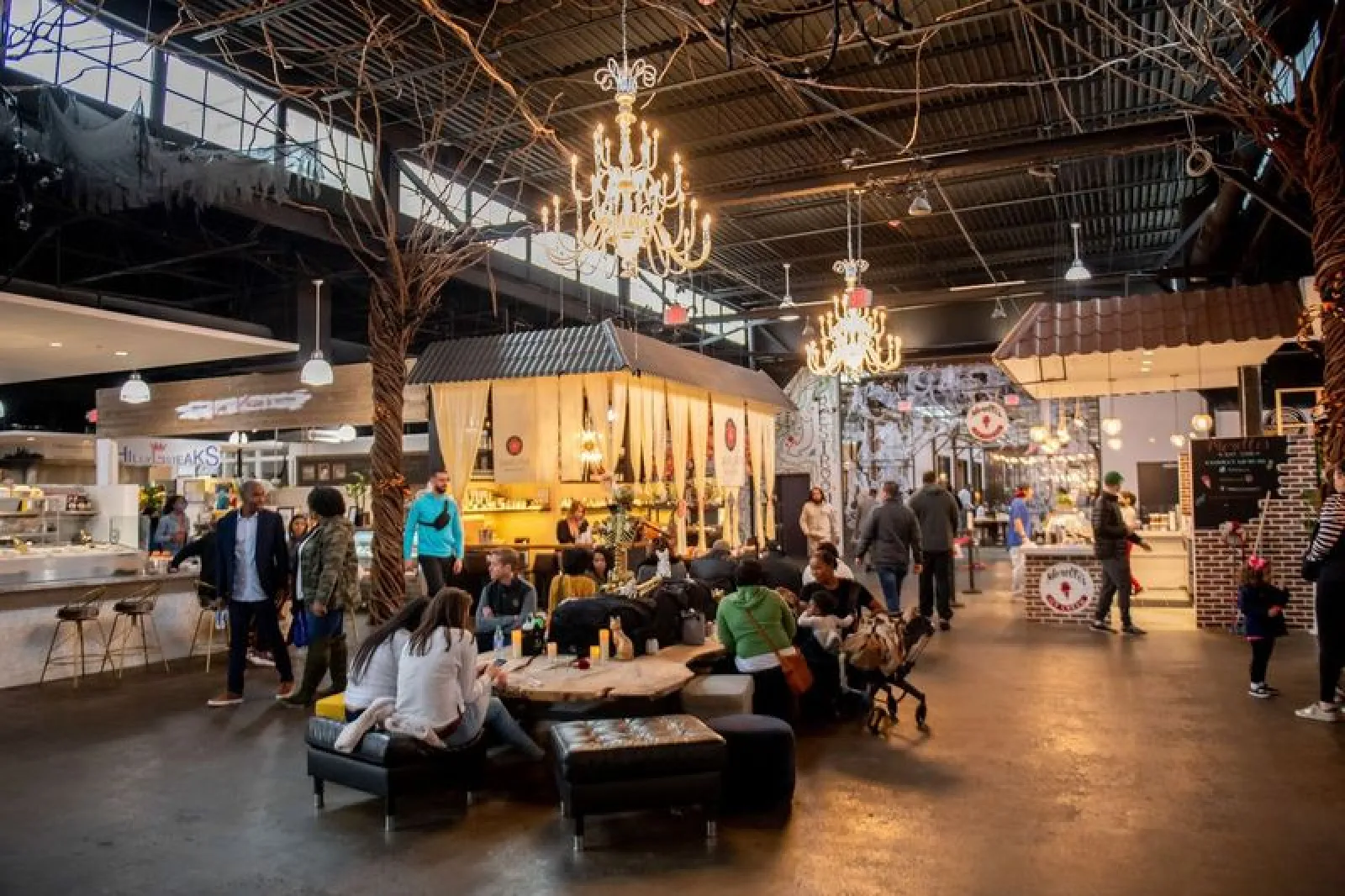 Indoor food market with people dining and walking under chandeliers and high ceiling lighting.