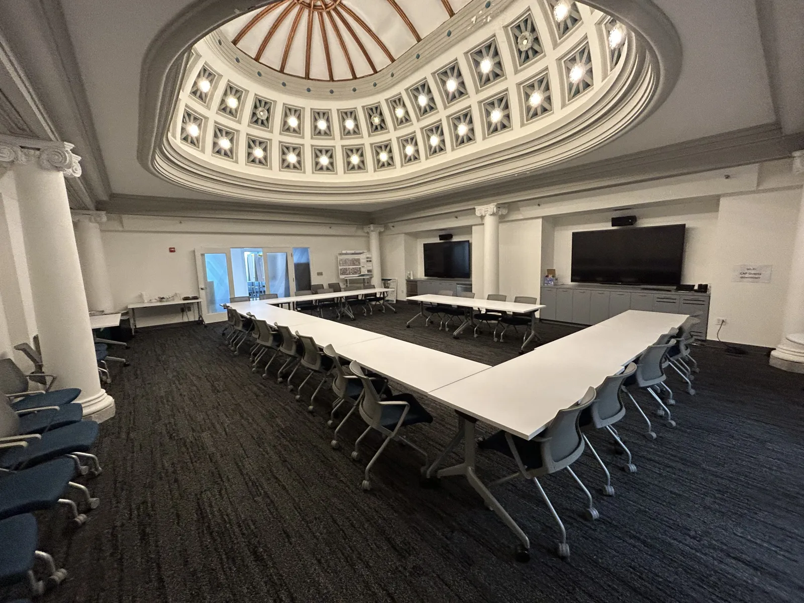 Conference room with U-shaped tables and chairs under a decorative domed ceiling with natural light.
