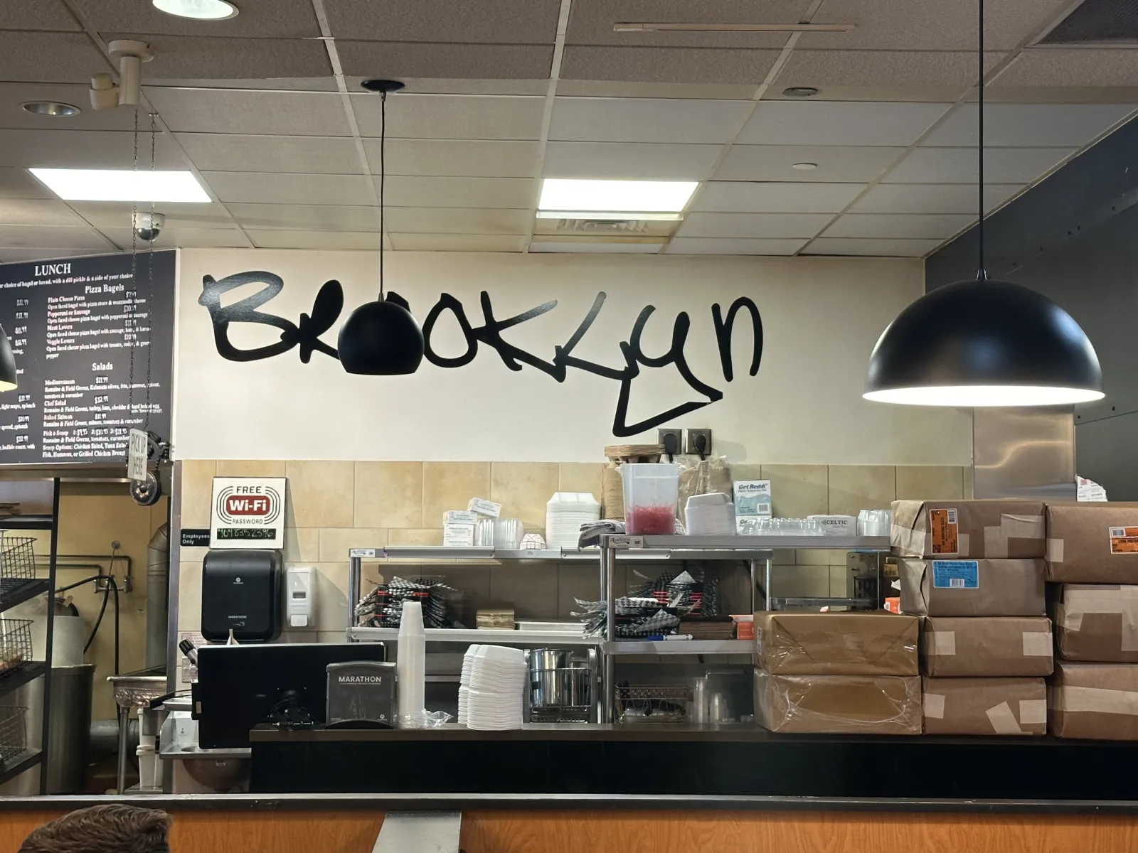 Interior of a Brooklyn restaurant with shelves, stacked boxes, pendant lights, and handwritten wall text.