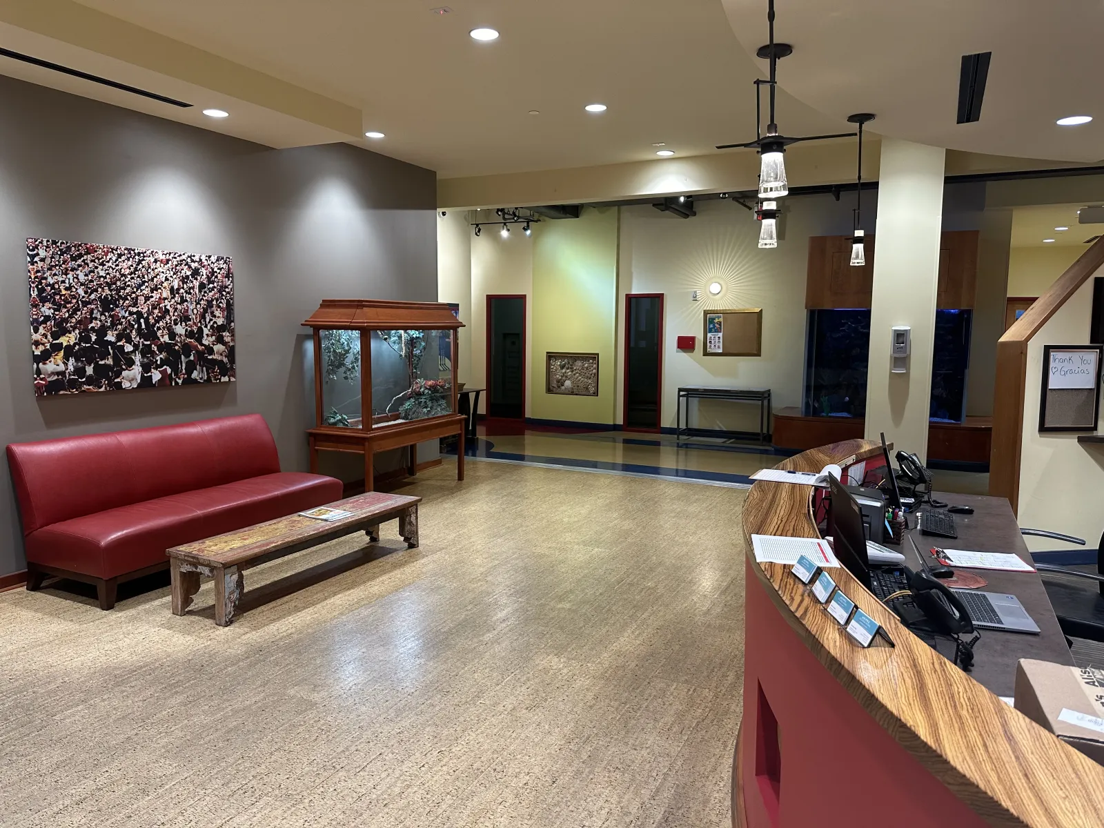 Modern reception area with red couch, wooden bench, fish tank, and curved wood desk with computers.