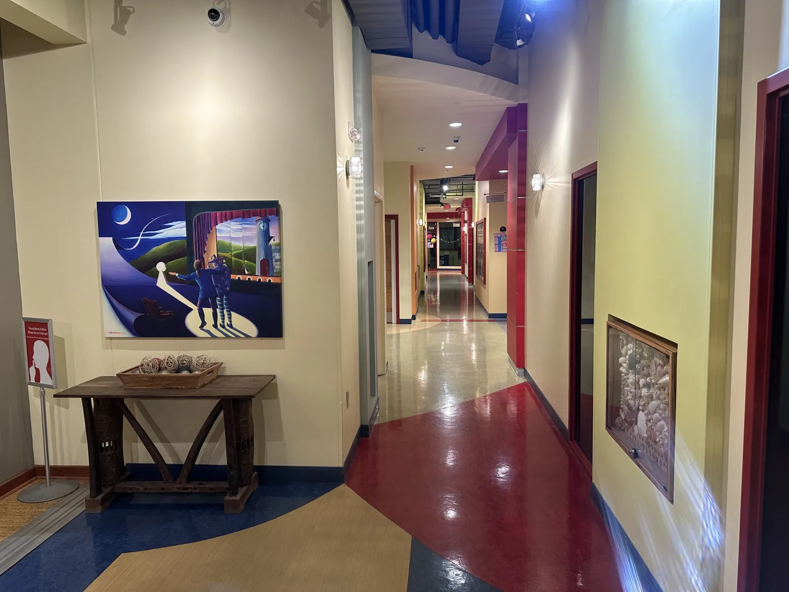 Colorful hallway with polished floors, artwork on the walls, and a wooden table with decorative items