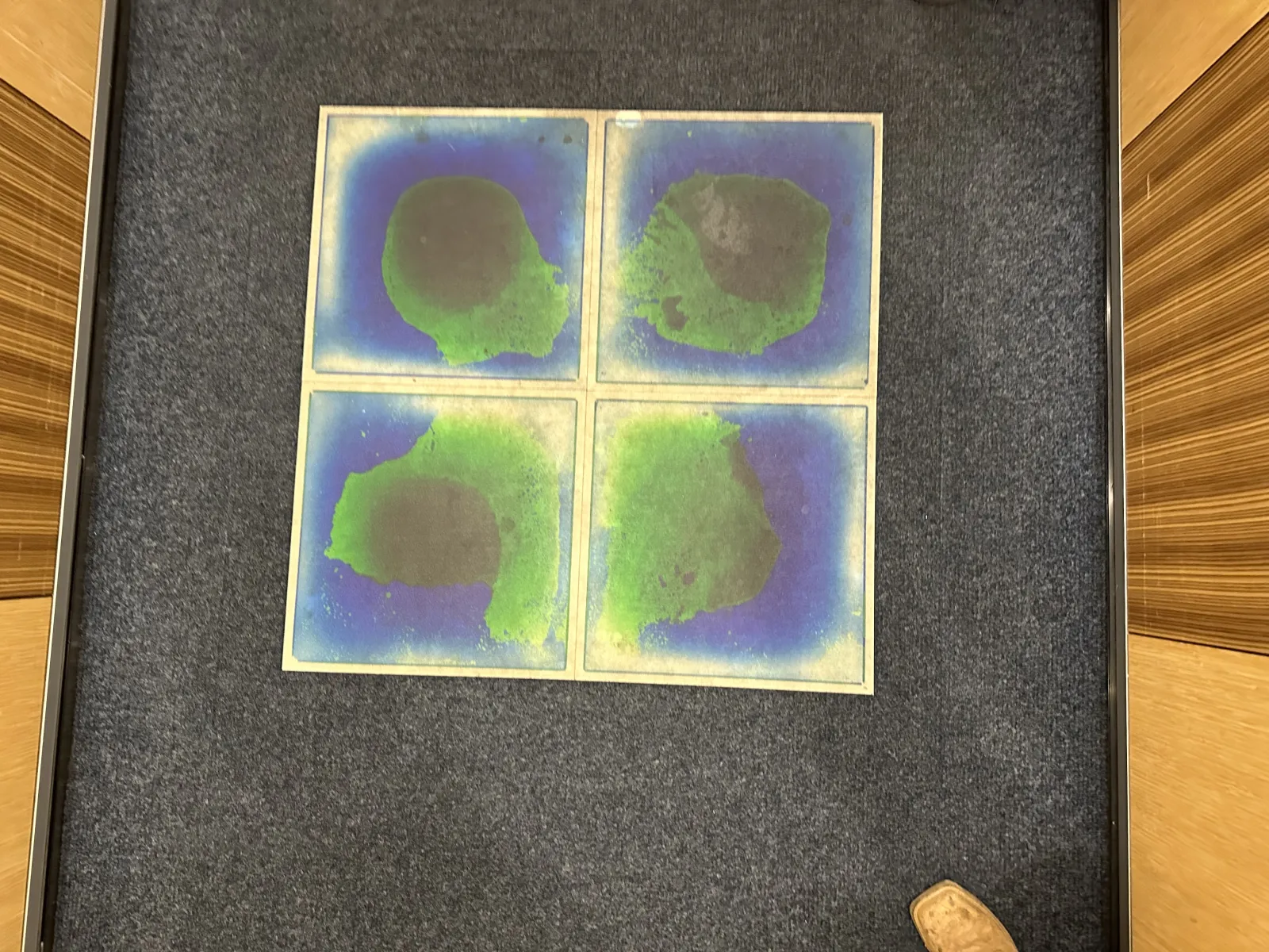 Four abstract watercolor paintings with green and blue hues arranged in a square on a gray carpeted floor.