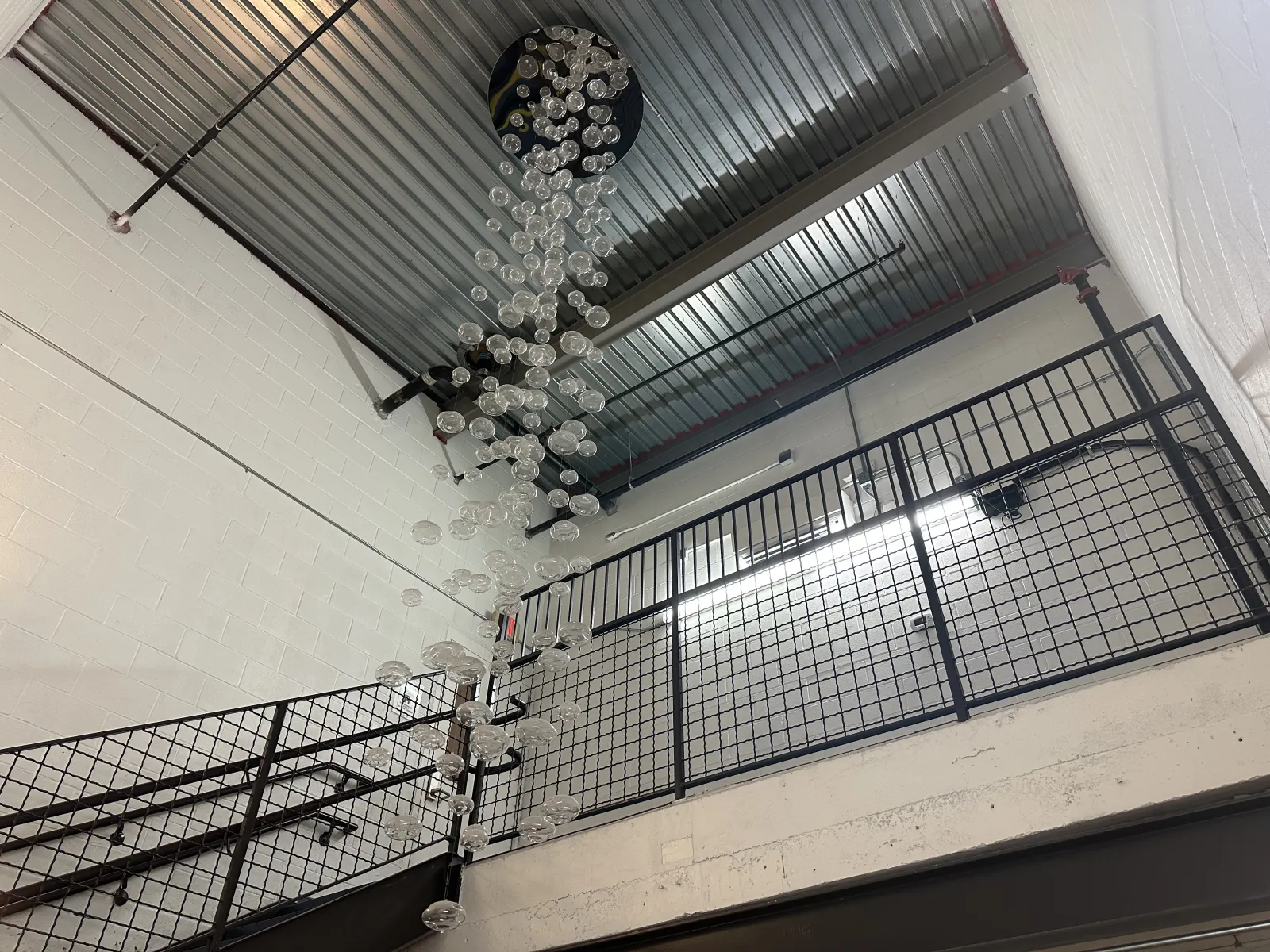 Modern indoor stairwell with metal railings and hanging glass bubble chandelier under industrial ceiling.