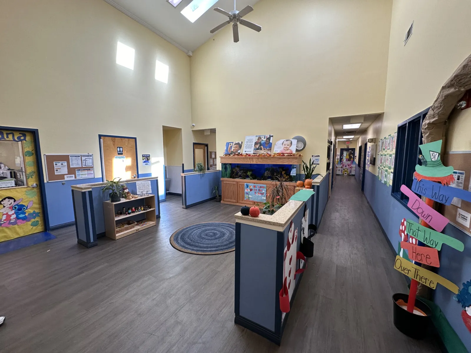 Bright and spacious childcare center hallway with colorful decorations, aquarium, and directional signposts.