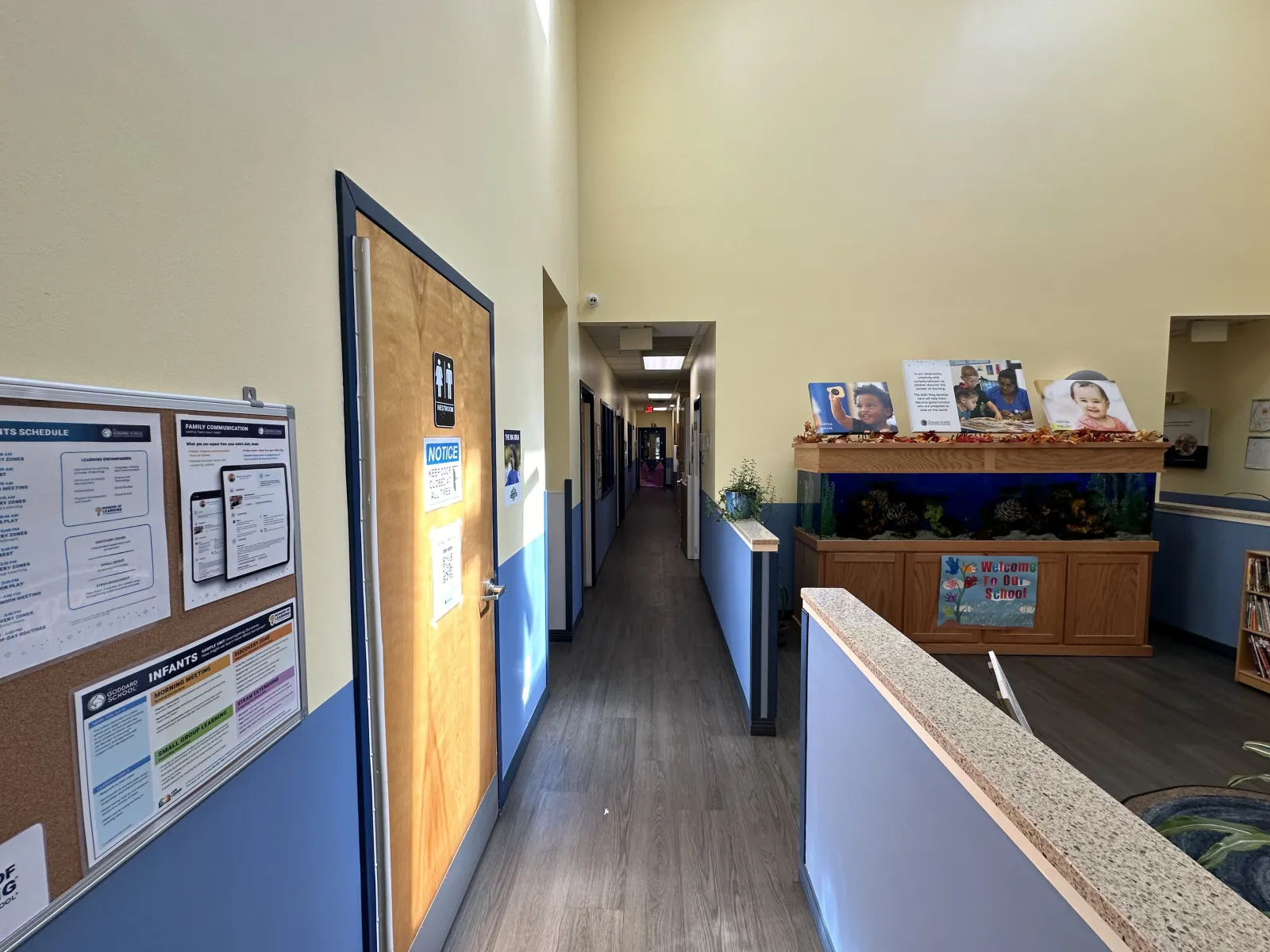 Interior hallway of a childcare facility with informational boards, wooden doors, and an aquarium display.