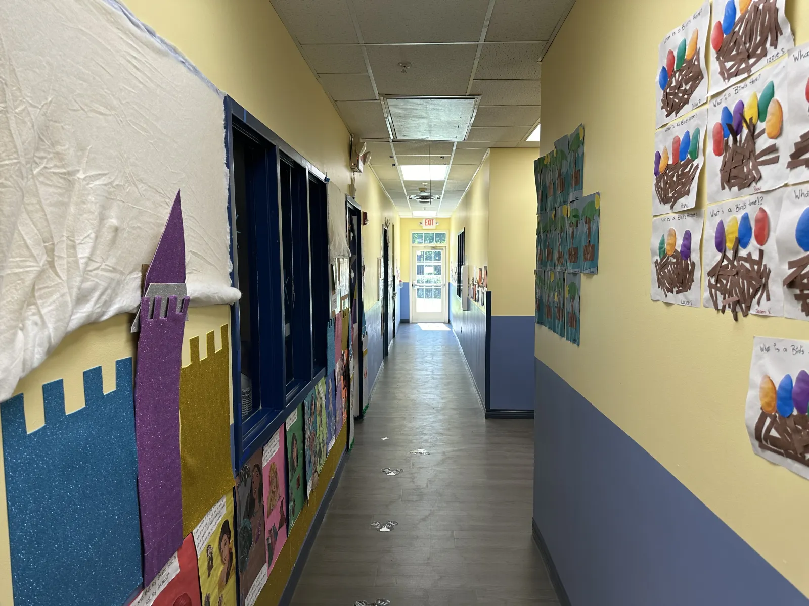 Bright school hallway decorated with student artwork on walls and a view to a glass exit door at the end.