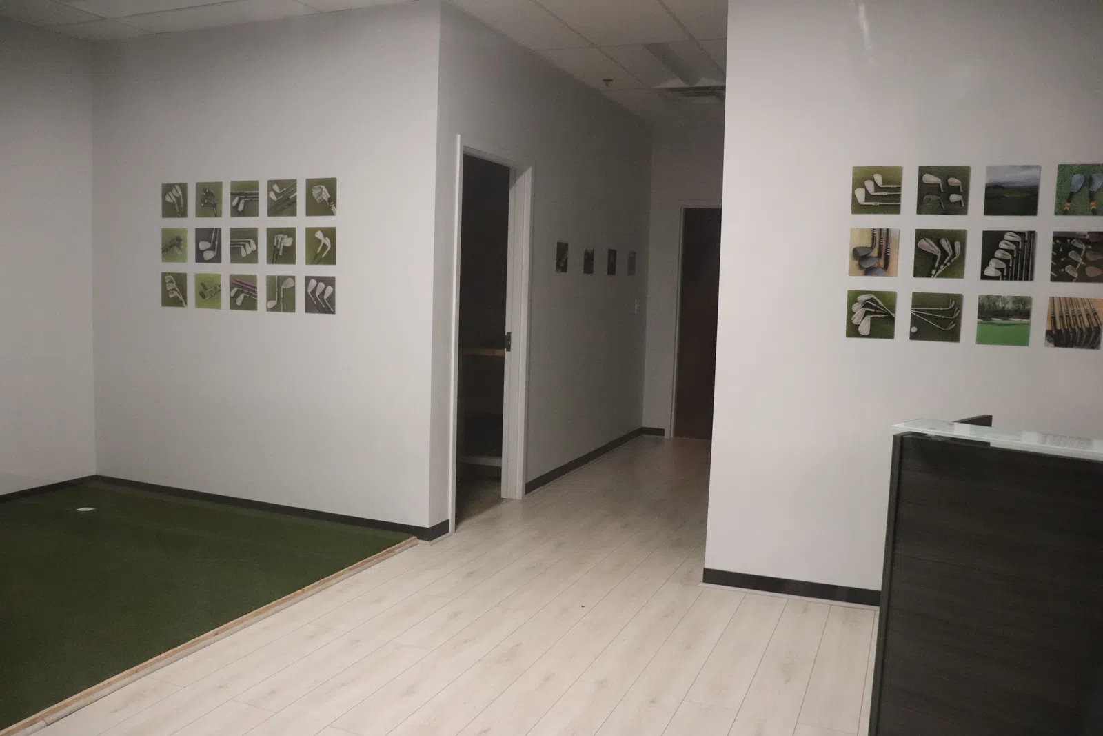 Modern indoor golf practice area with green turf, white walls, and golf club images displayed on walls.