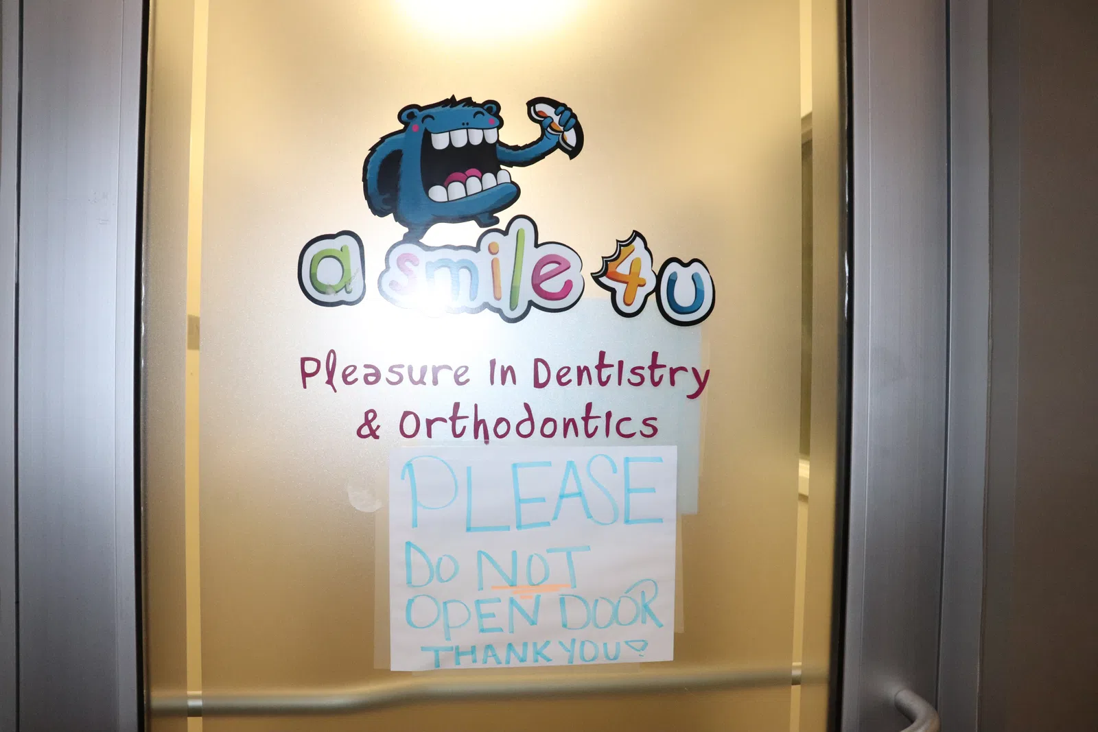 Dentistry office door with colorful logo 'a smile 4 u' and a sign asking not to open the door.
