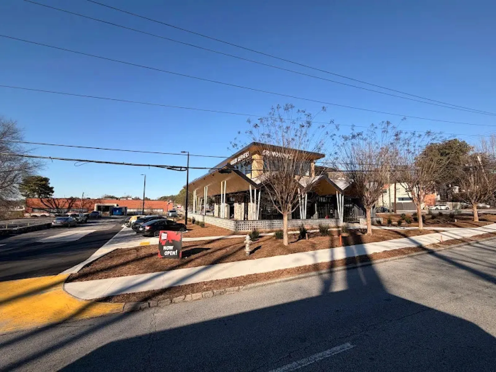 Modern restaurant building with large windows under clear blue sky and parking lot on a sunny day.