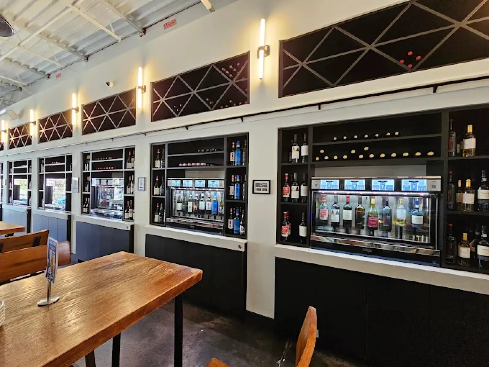 Modern wine tasting room with wooden tables and automated wine dispensers against white walls.