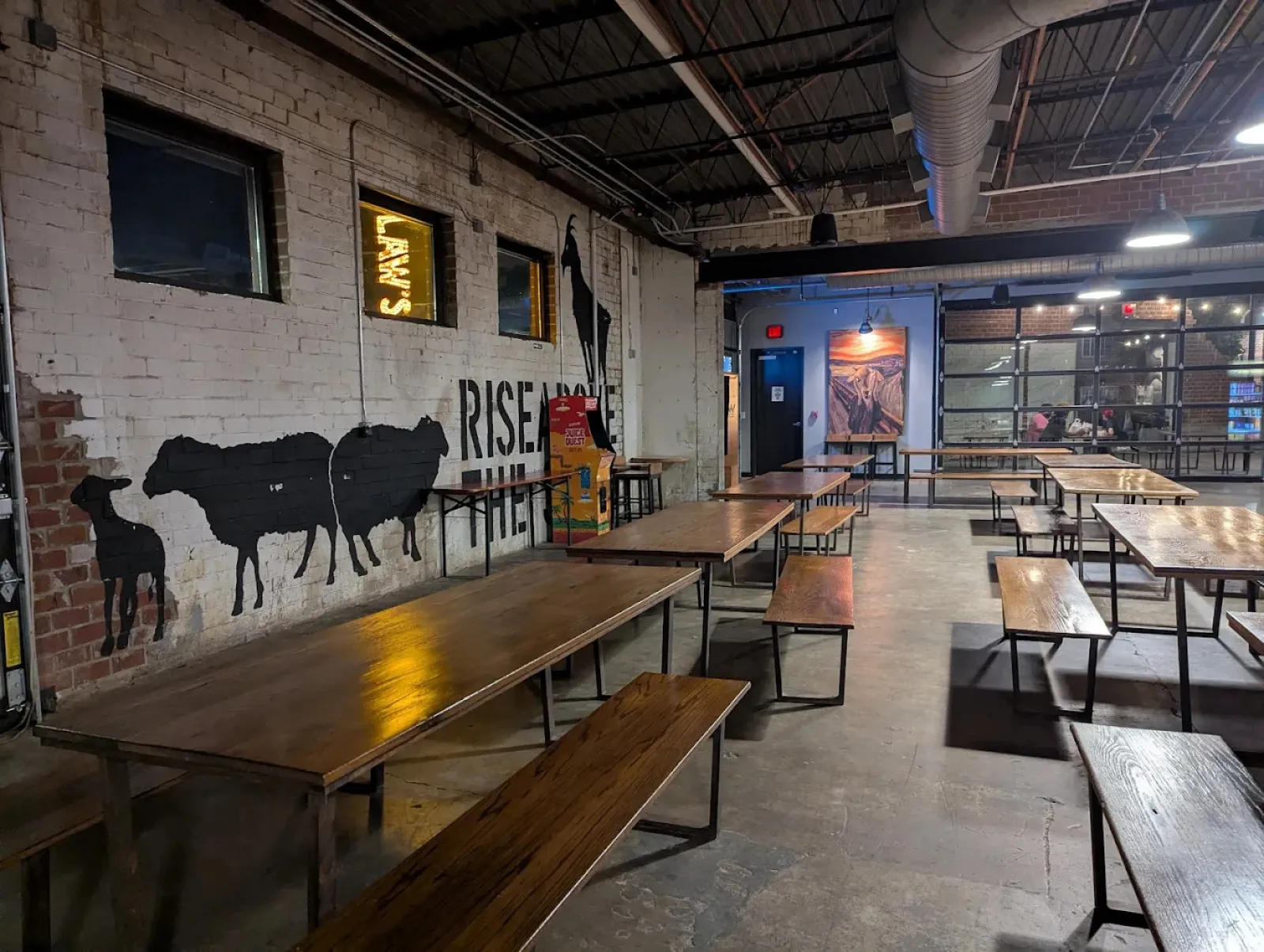 Interior of a rustic industrial dining area with wooden tables, benches, and animal murals on brick walls.