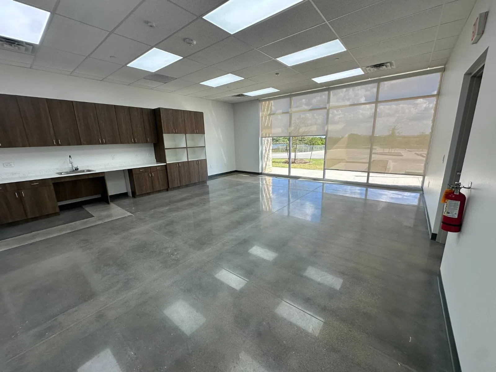 Empty modern room with polished concrete floor, wooden cabinets, large windows, and ceiling lights.
