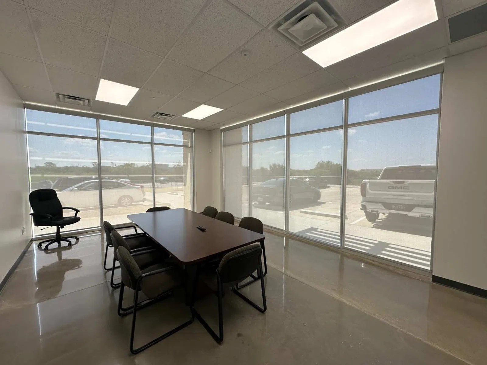 Modern conference room with large windows, a dark wooden table, black chairs, and polished concrete floor.