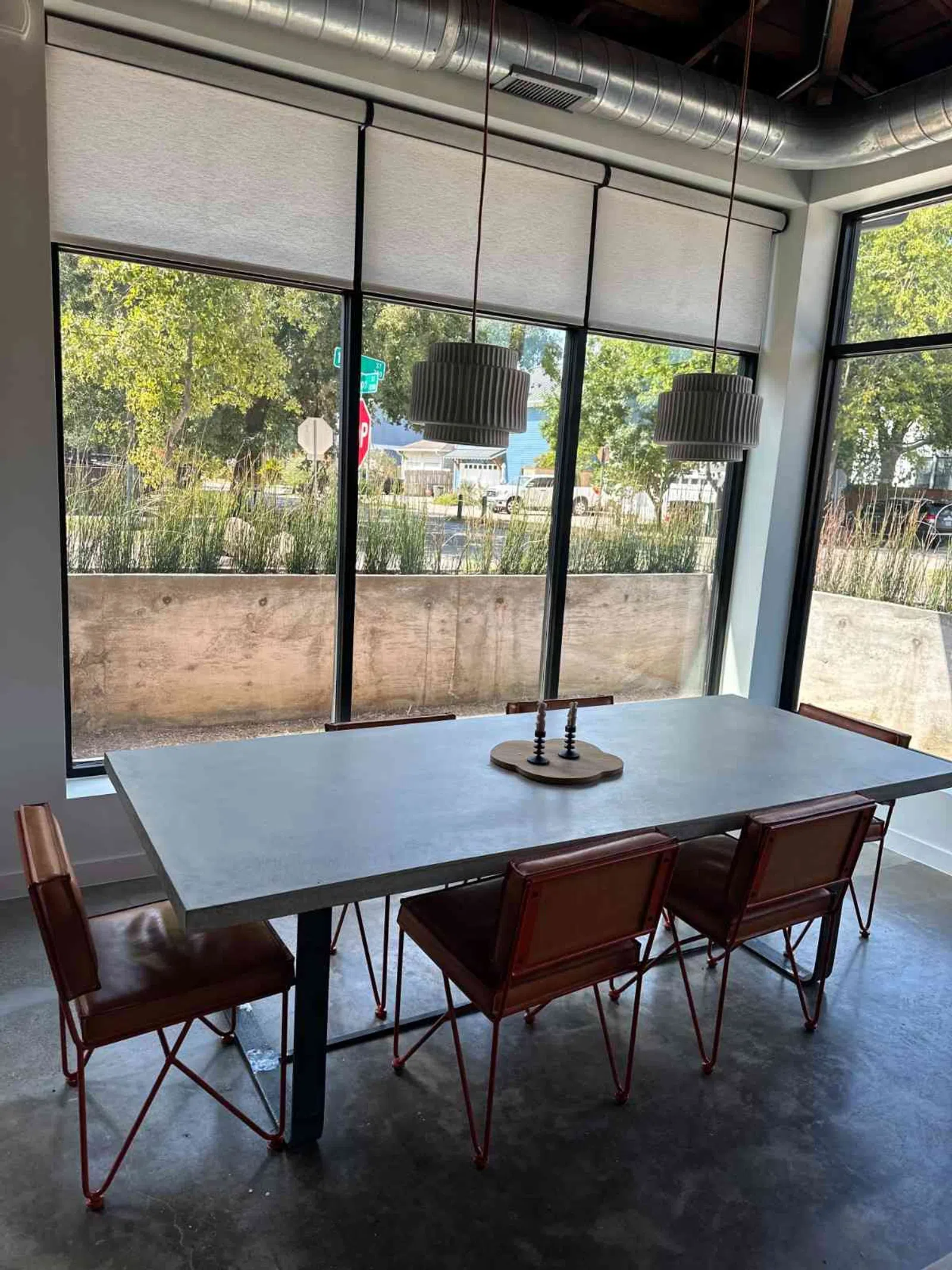 Modern dining area with gray table, brown metal chairs, pendant lights, and large windows with outdoor view.