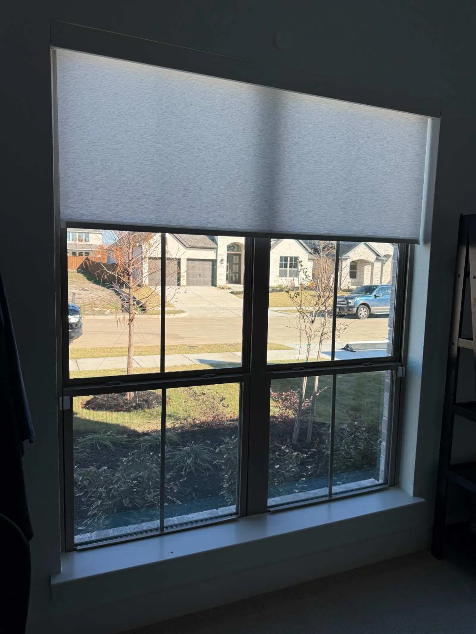 View through a large window with a partially lowered white roller shade lighting the room during daytime.
