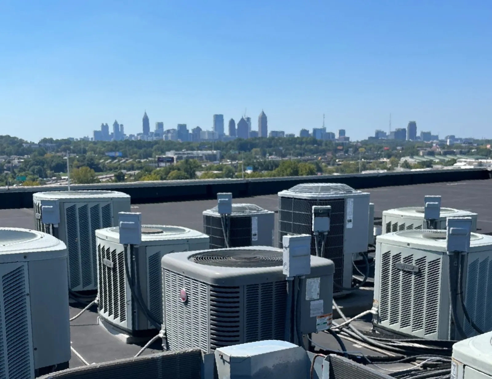 Multiple rooftop HVAC units installed on a building roof with the city skyline under clear blue sky