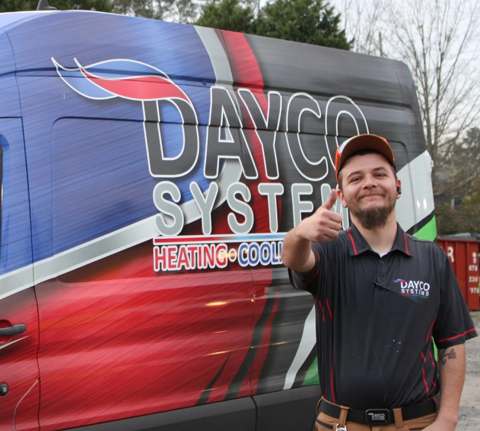 Smiling technician in Dayco Systems uniform gives thumbs up next to colorful Dayco Systems HVAC service van.