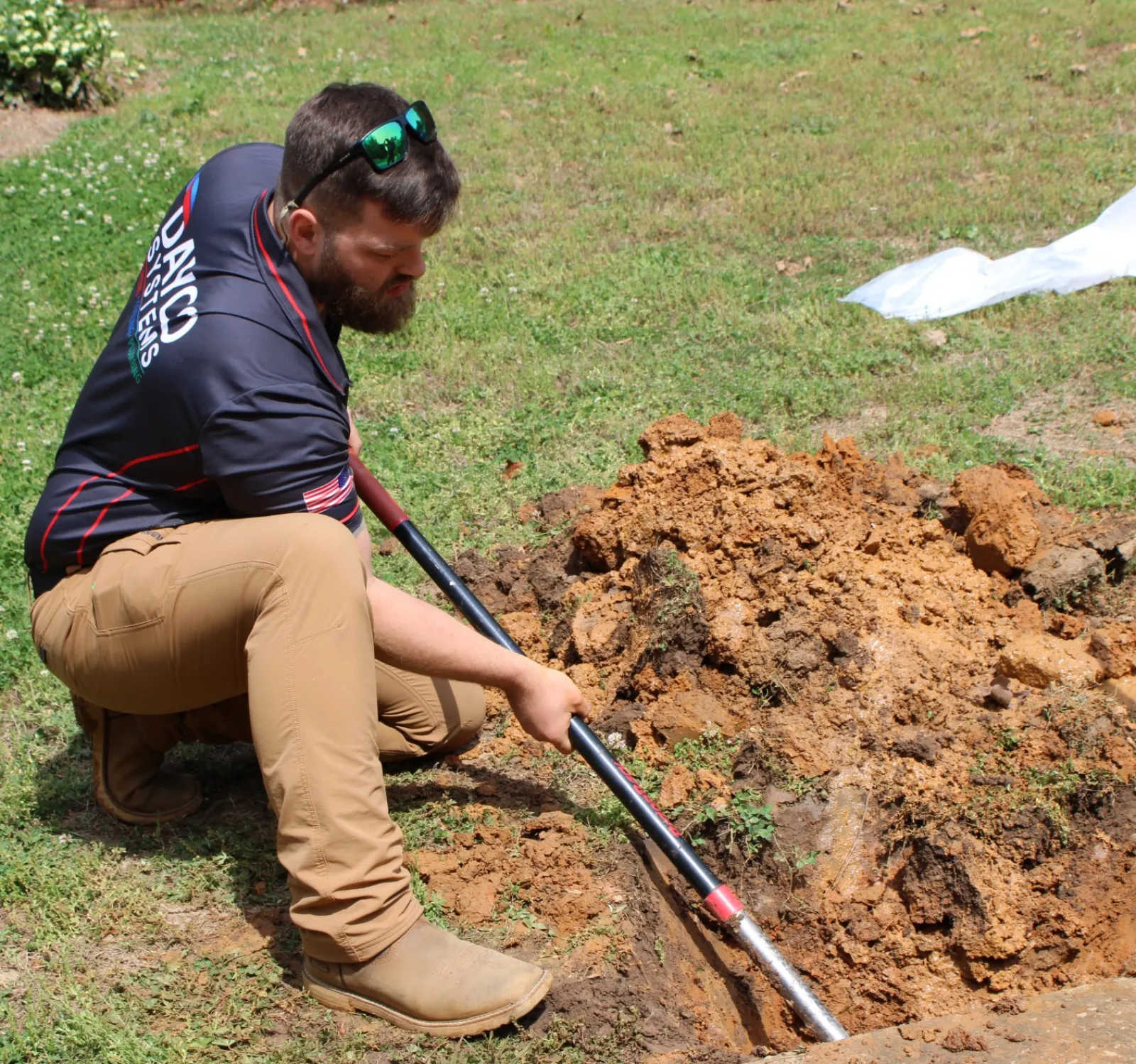 Man in work clothes digging a hole in the ground with a shovel on a grassy area to fix plumbing leak during daytime