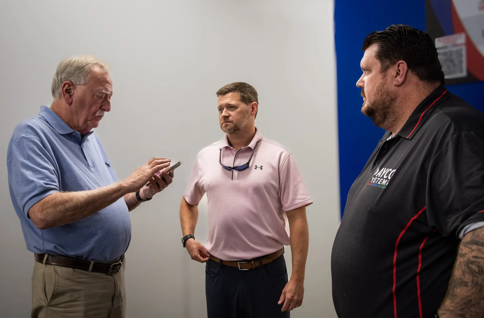Three men having a serious conversation indoors, one using a smartphone, others listening attentively.