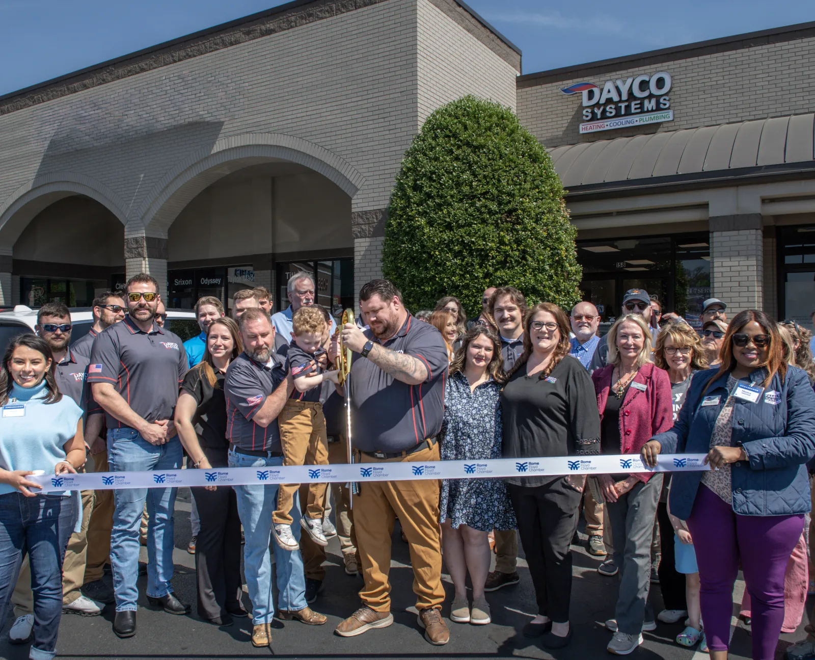 Group of people at a ribbon-cutting ceremony outside Dayco Systems building on a sunny day.